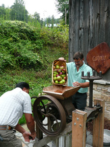 Joseph Cathey pours apples into a cider press while a helper turns the wheel.